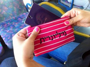 ארנק ורוד עם כיתוב שחור "מיליונרית" אצל אישה שיושבת באוטובוס