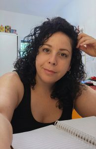 אישה מחייכת עם שיער מתולתל כהה וטנק טופ שחור. דיוקן עצמי יומיומי עם פנקס. מערכת MEETMEEP לניהול נוכחות דיגיטלית לעצמאיים